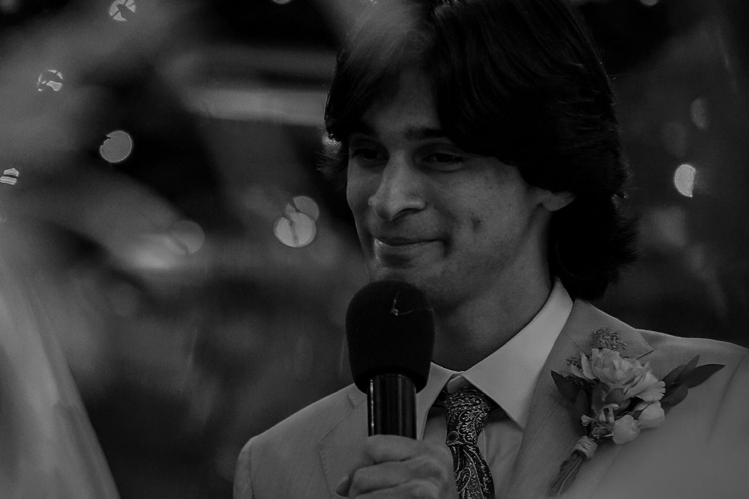 Close up of the groom as he looks into his brides eyes as he says his vows to her with love in his eyes, a soft playful smile on his lips.