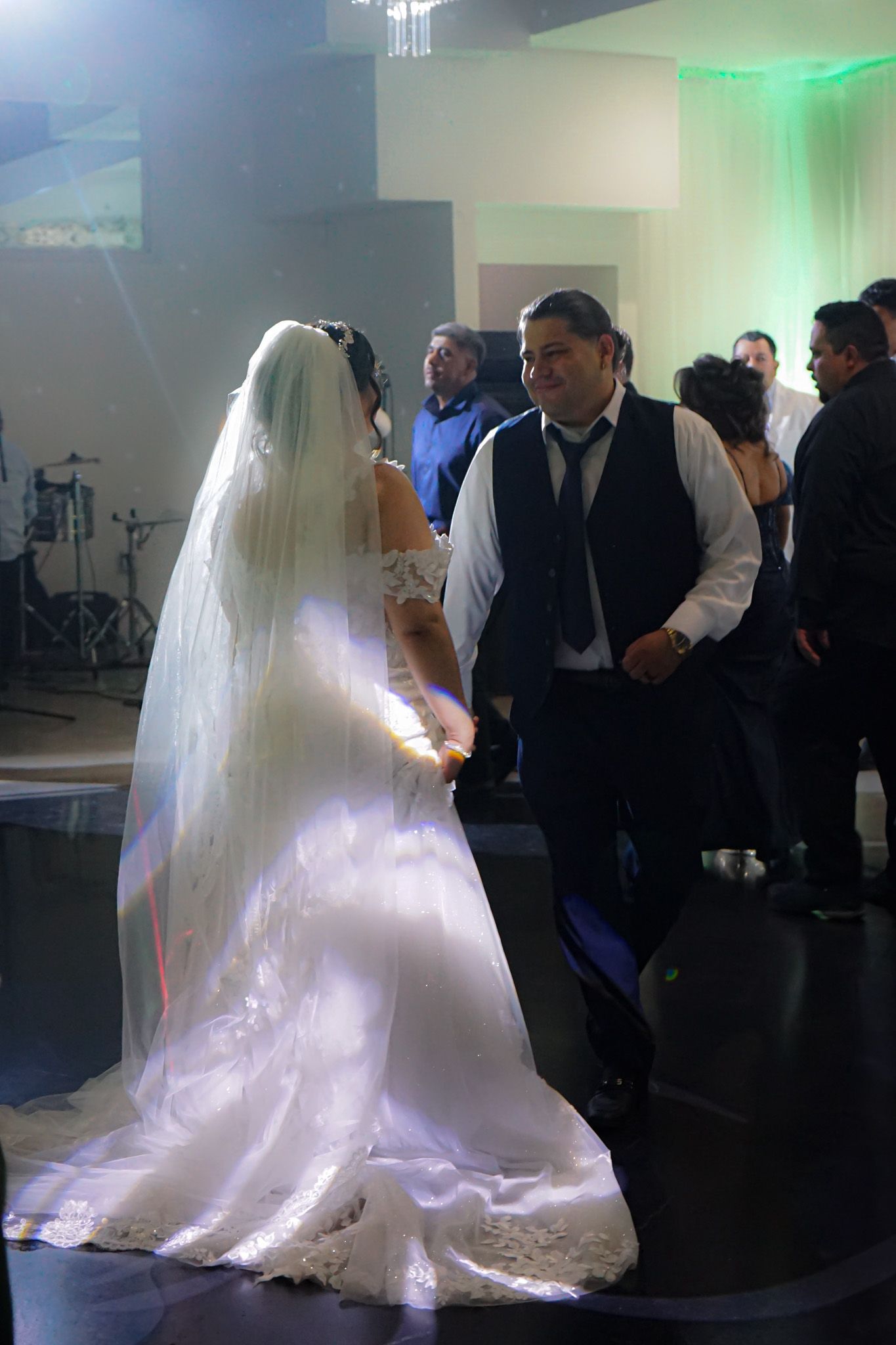 Bride and groom dancing joyfully at their wedding reception, smiling at each other under glowing lights.