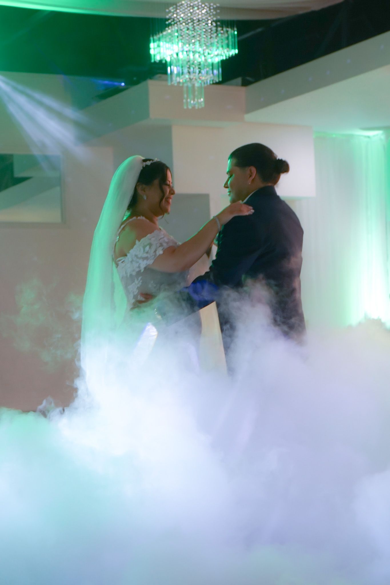 Newlyweds in a close embrace while dancing at their wedding reception, laughing and celebrating their first dance together.