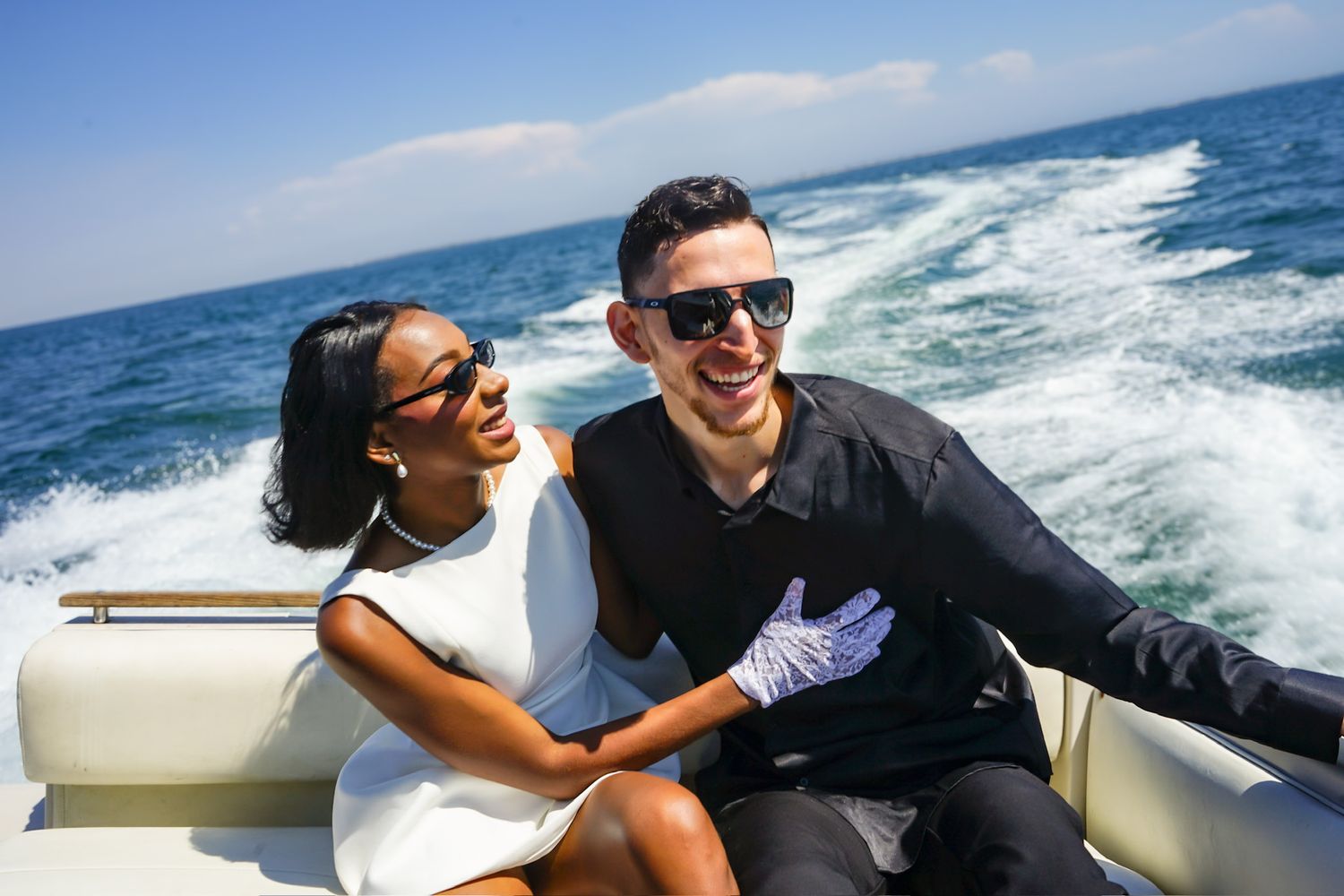 Engaged couple laughing together during engagement shoot while riding in the back of a speed boat.