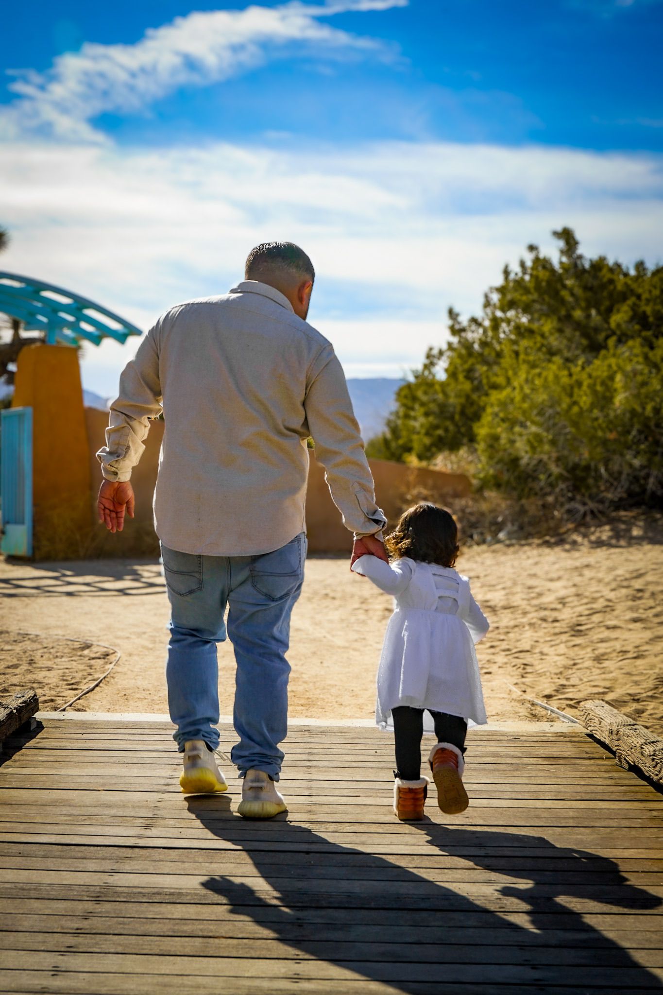 Father and daughter walking hand in hand away down a path with the warm sunlight beaming on them highlighting their shadows.