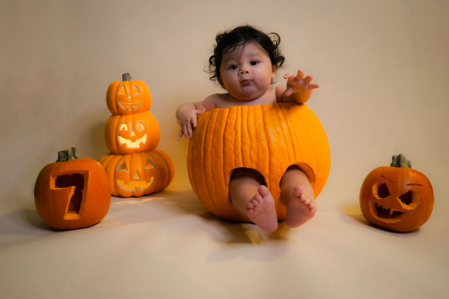 Studio session of a milestone month for a 7 month old baby boy sitting in a hollowed out pumpkin surrounded by smaller pumpkins.