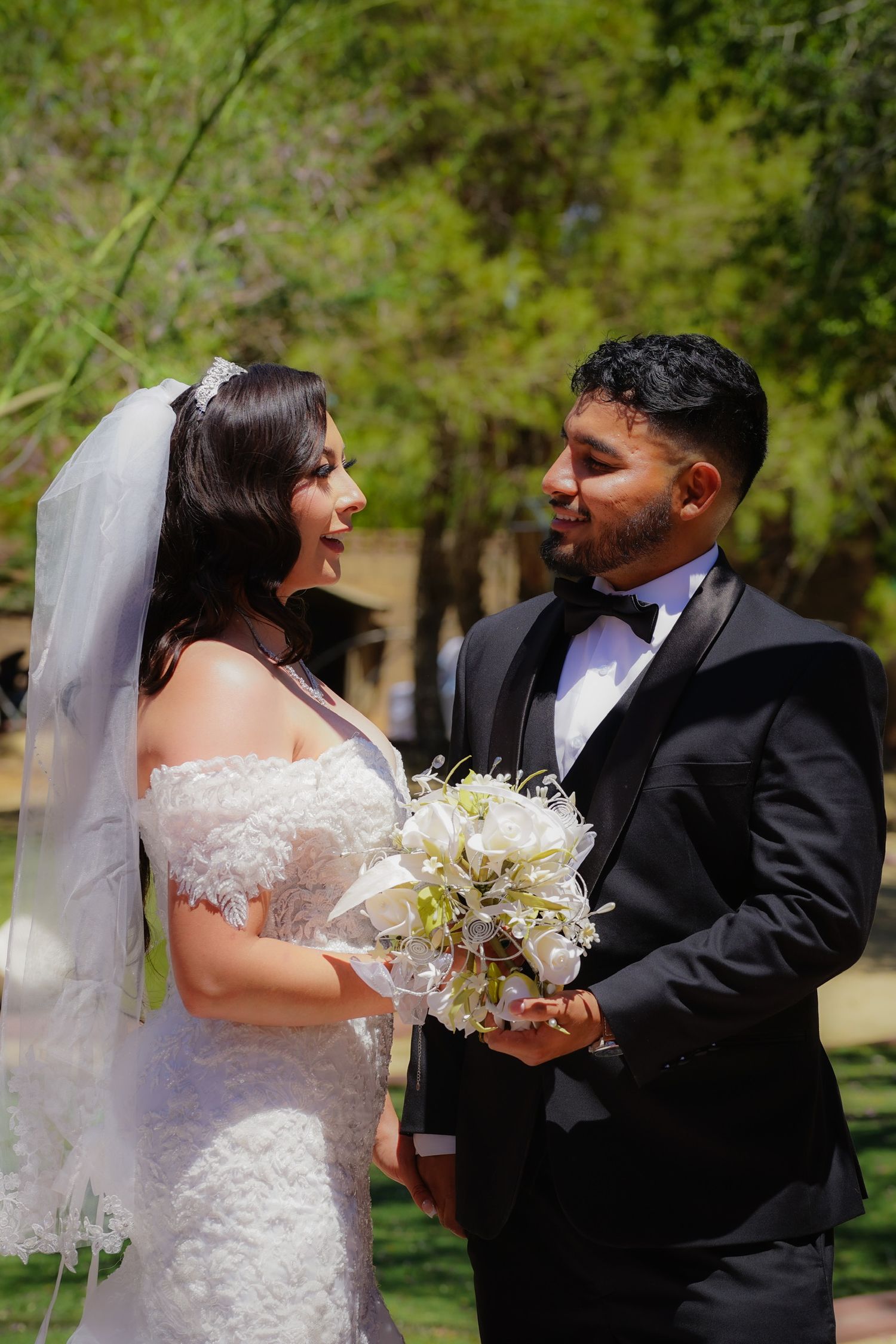 Bride and groom standing outdoors after their wedding, holding hands and looking lovingly into each other’s eyes.