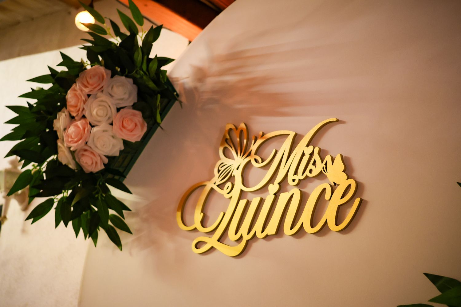 Close up of decorative backdrop with the words in gold saying Mis Quince complimented by butterfly elements and pink florals.