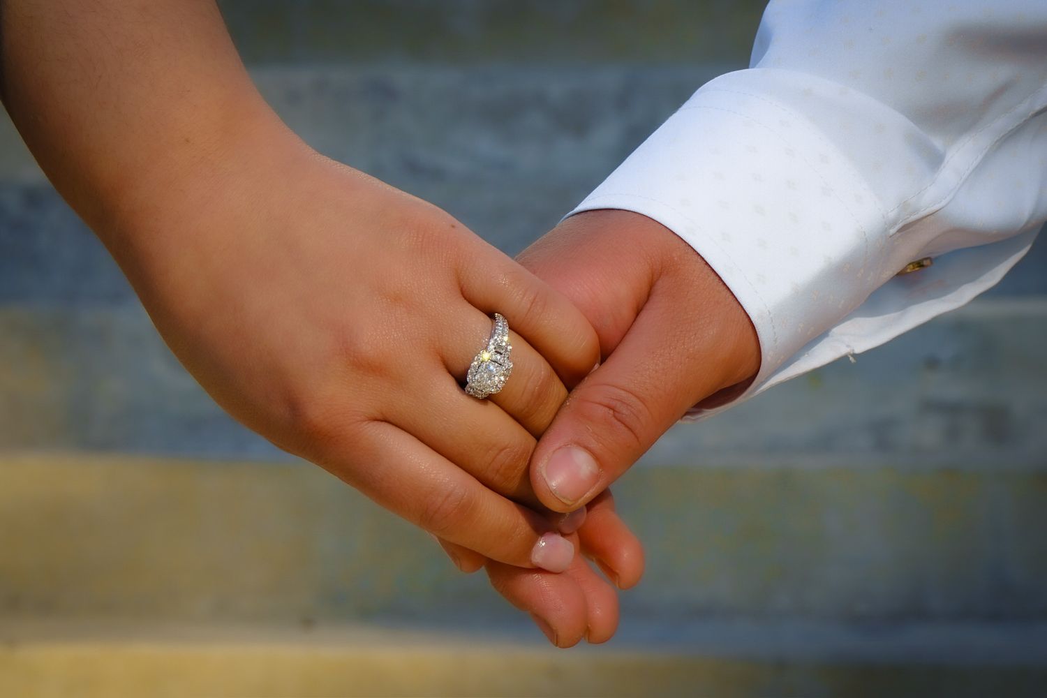 Close up of the couples hands holding one another gently, with the engagement ring shining brightly in the glow of the daylight.