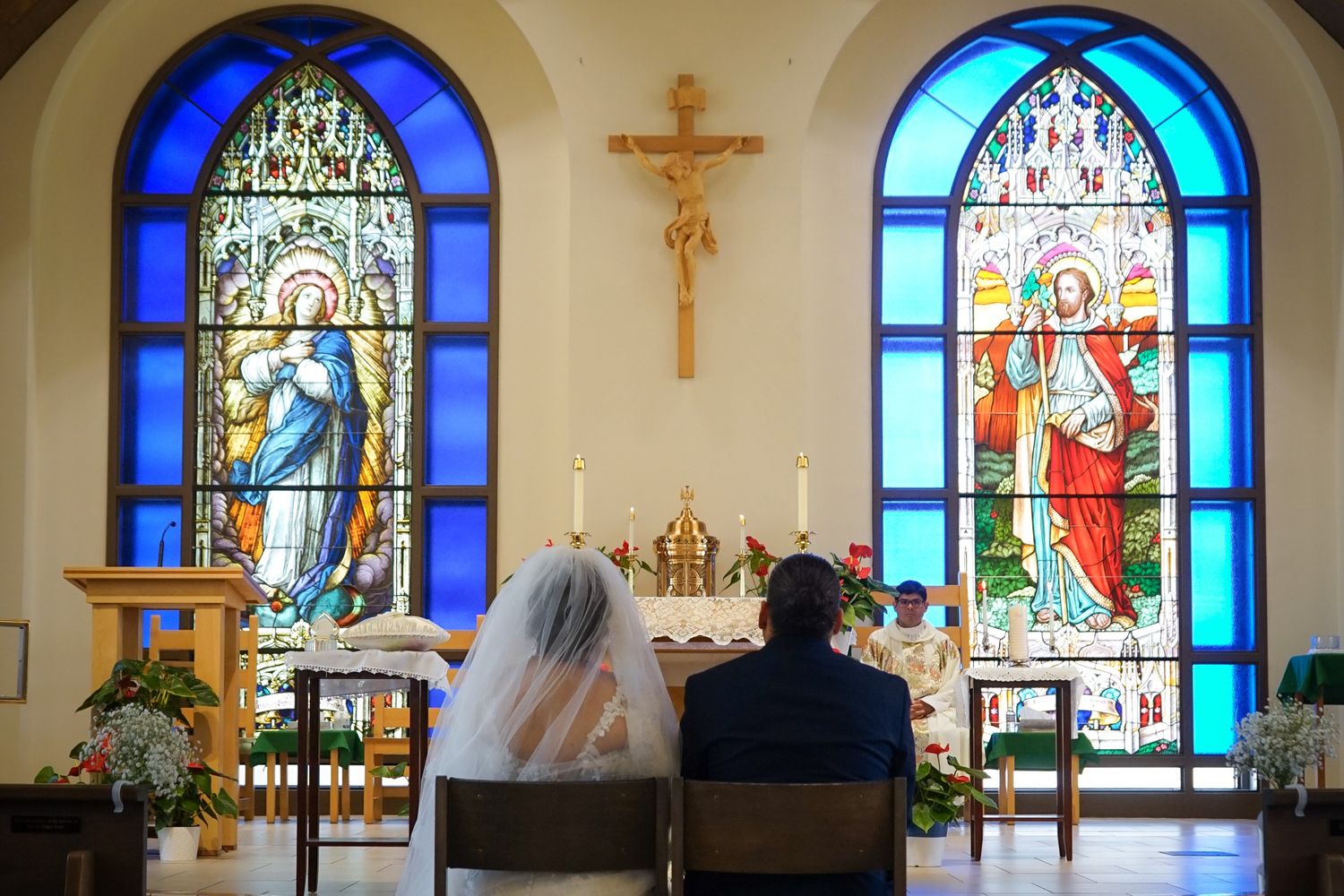 Aisle view of couple during church wedding ceremony sat together facing the altar.