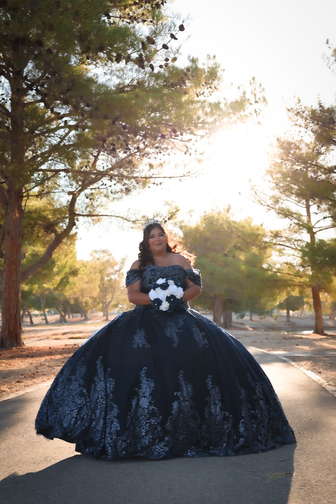 Girl in a blue quinceañera dress posing near a lake before her celebration, sunlight reflecting off the water and highlighting her gown.