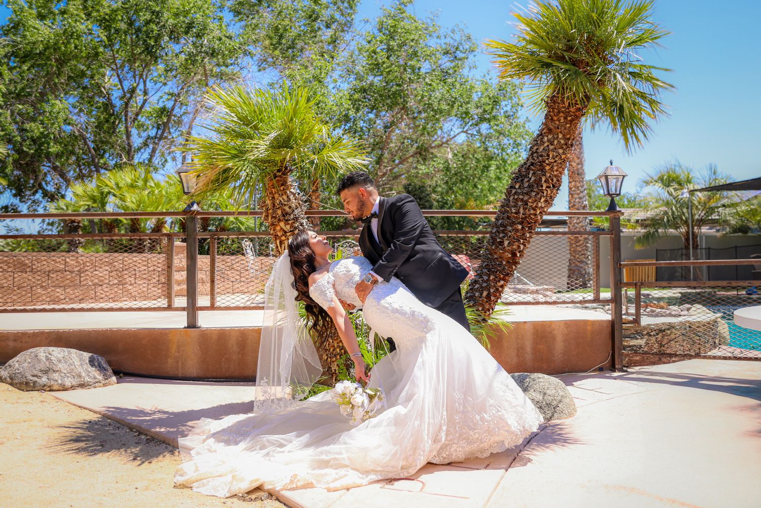 Groom dips the bride outdoors in bright sunlight, the couple smiling at each other.