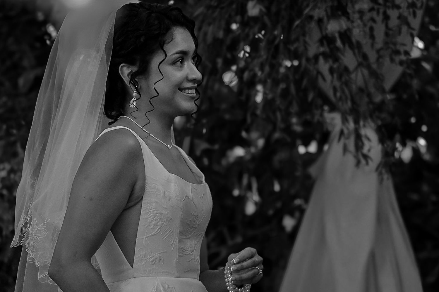 Close up of the bride as she watches her groom deliver his vows to her, she smiles widely wearing her beautiful wedding dress and veil.