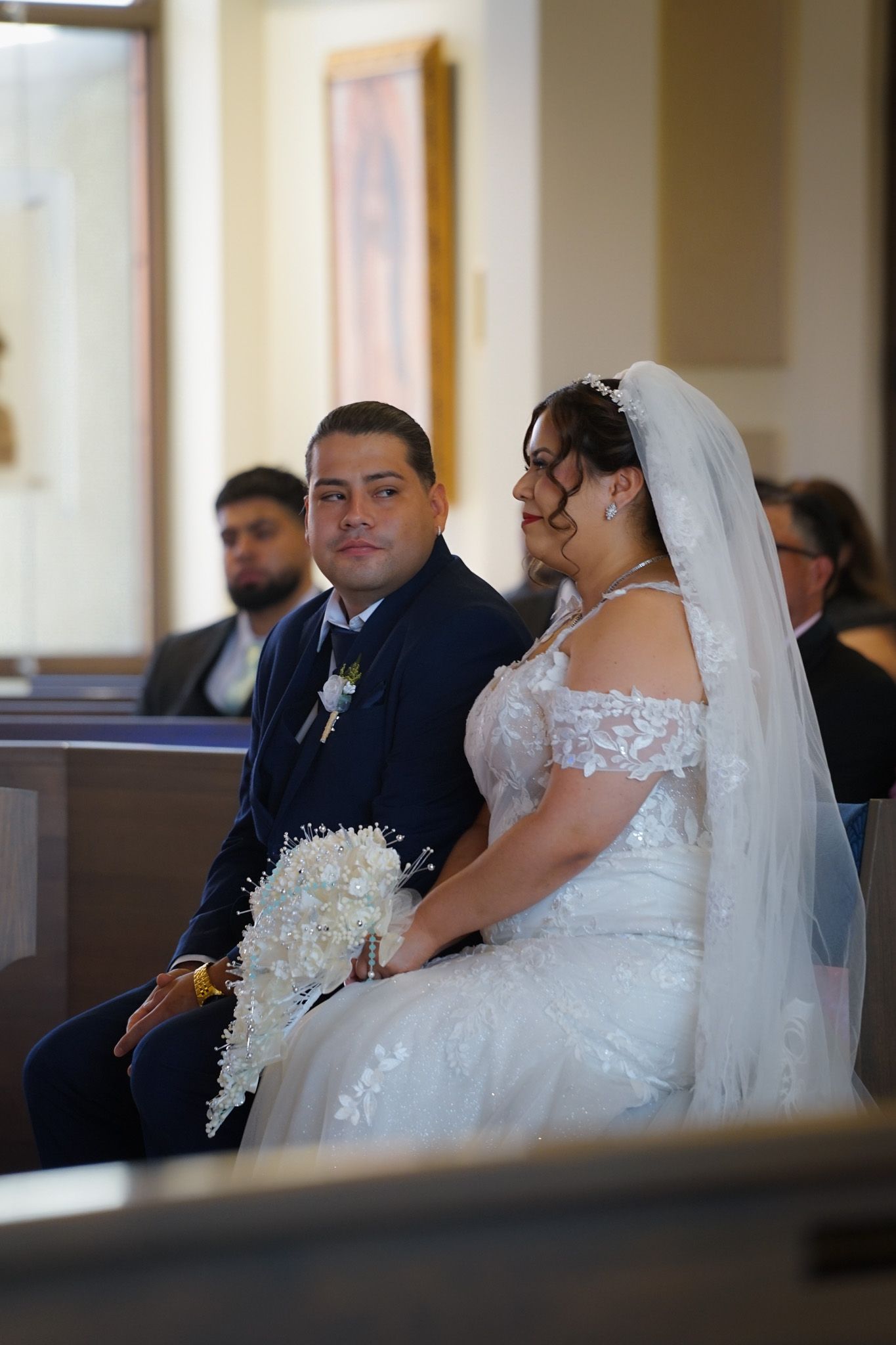 Bride and groom sitting together inside the church just after their wedding ceremony, smiling at the camera with the altar in the background