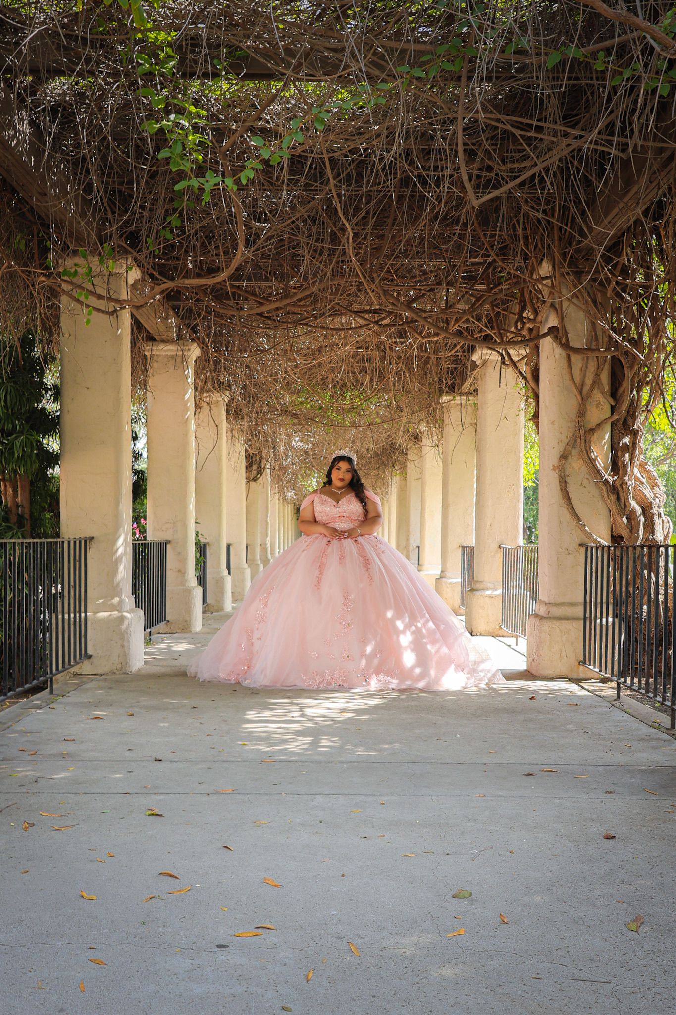 Quinceañera girl smiling in a pink ball gown outdoors before her celebration, sunlight highlighting her dress and joyful expression.