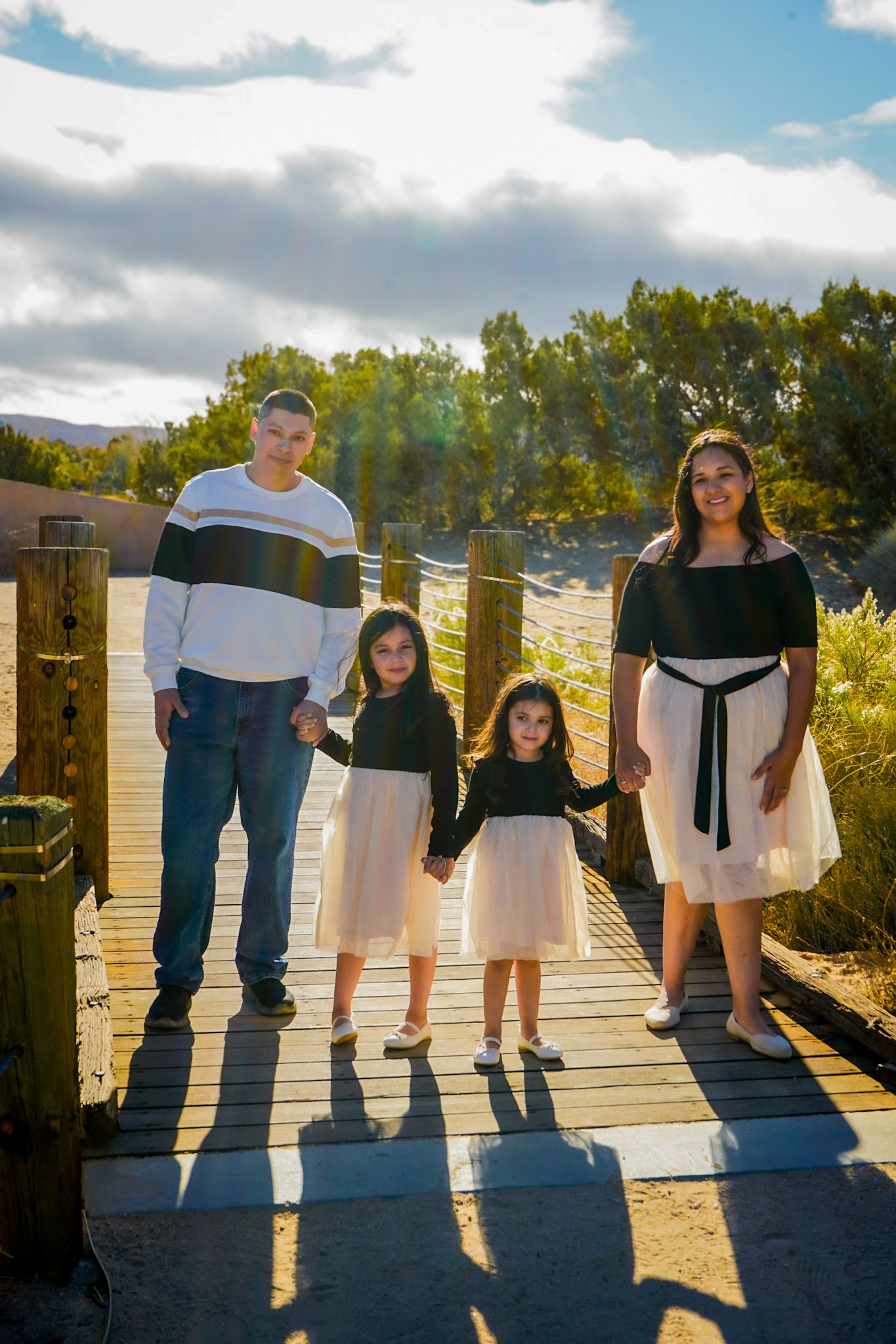 Family of four holding hands standing next to one another, the glow of the sun illuminating them from behind with a warm desert background.