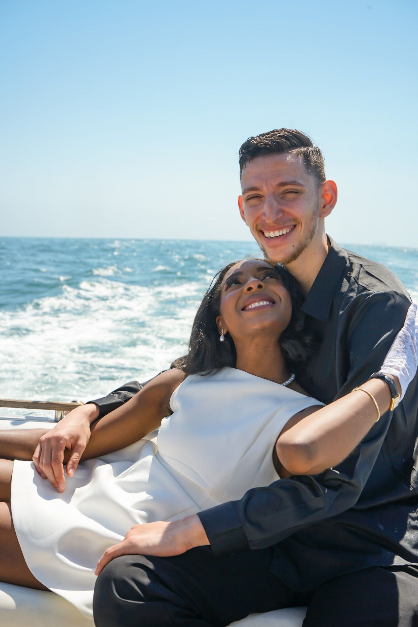 Engaged couple laughing together during engagement shoot while riding in the back of a speed boat.