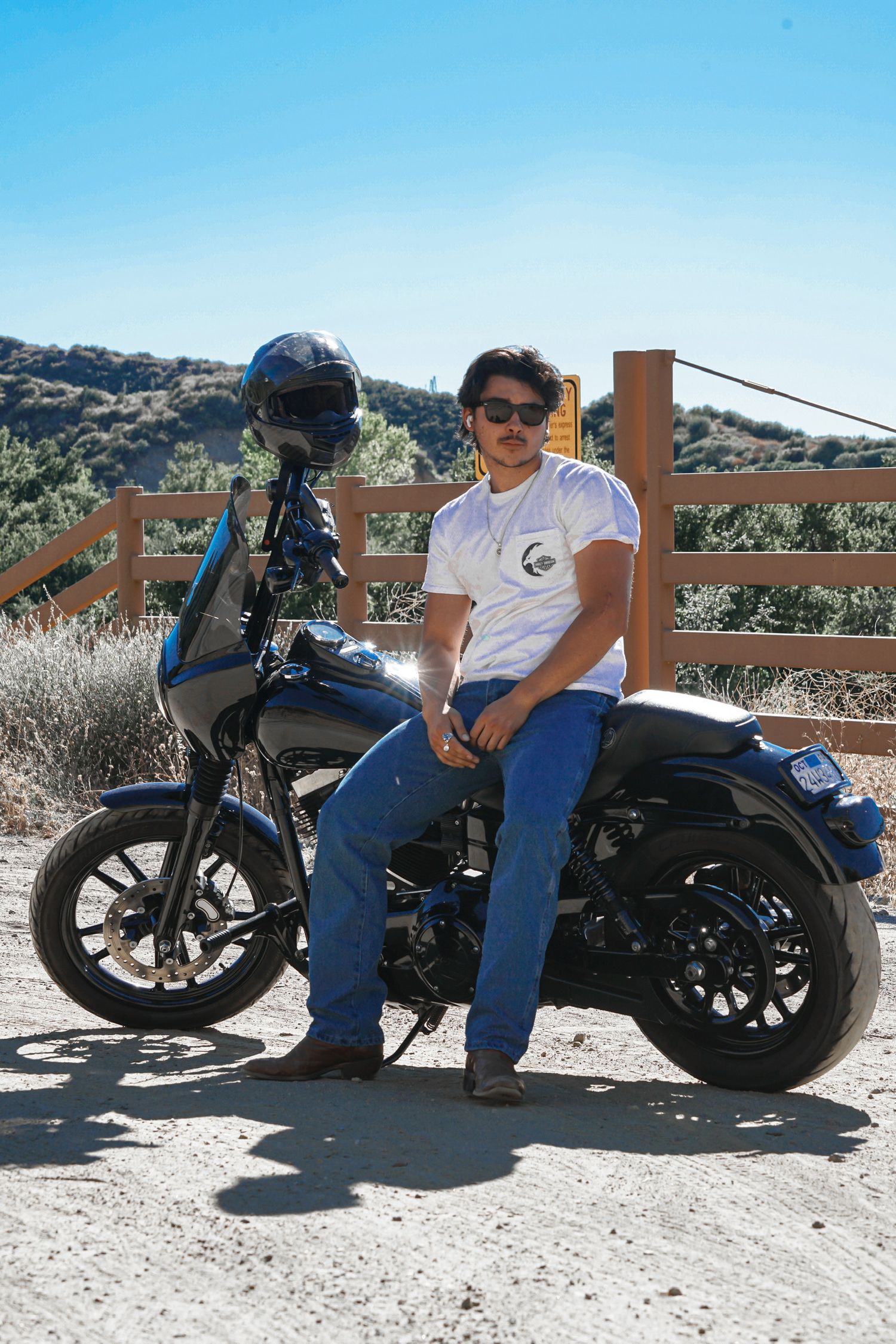 Motorcyclist posing for a portrait shot, leaning against his bike with a view of the mountains in the background.