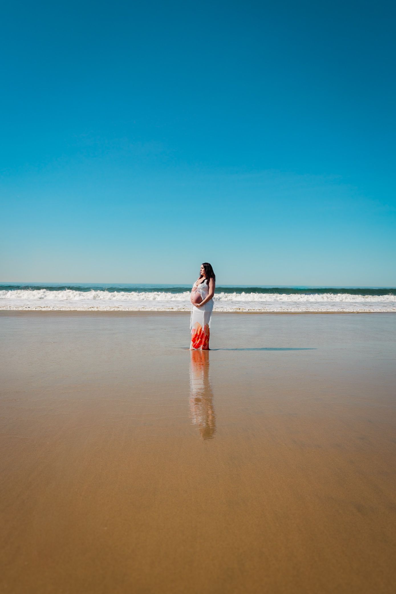 Pregnant mom standing near the water, looking off into the distance.