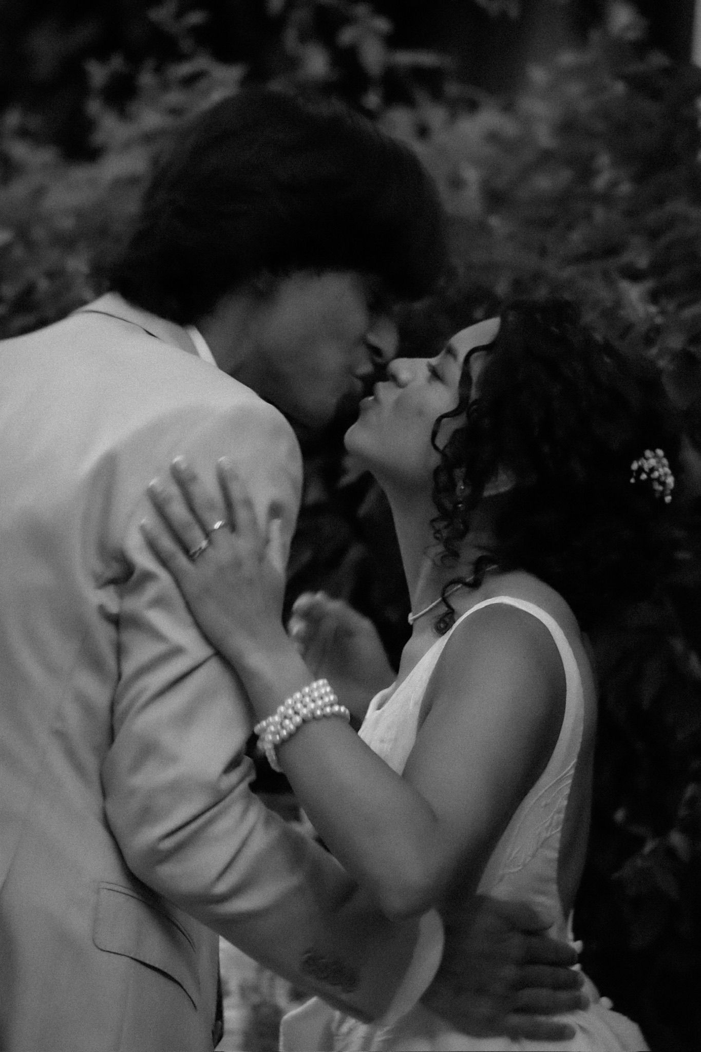 Newlyweds kissing after their wedding ceremony, the bride in a flowing gown and the groom in a suit, outdoors.