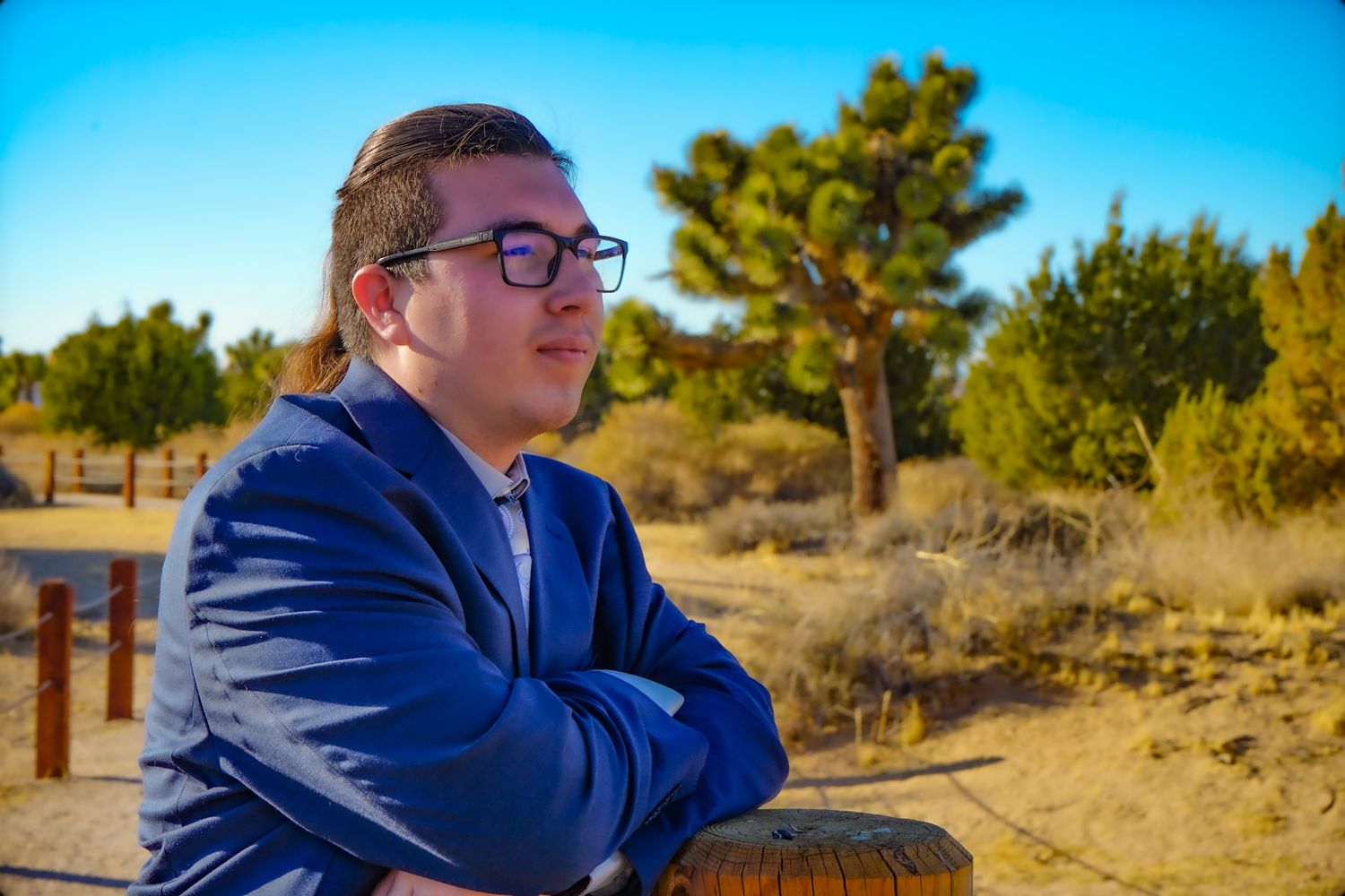 Side profile of a High school graduate wearing a blue suit standing off to the side on a bridge near Joshua Trees in a desert preserve.