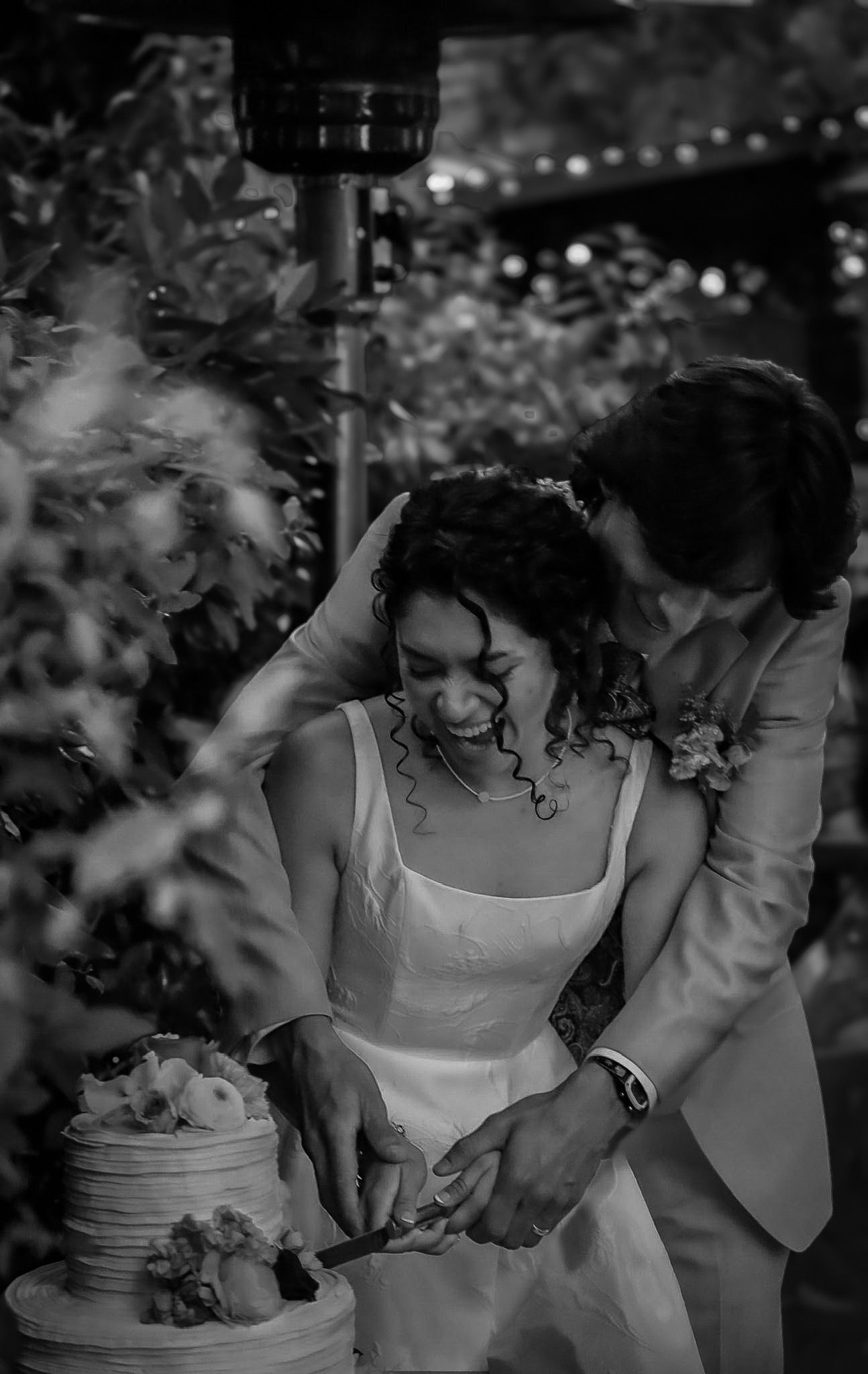 Black and white image of newlywed couple cutting their wedding cake together while laughing joyfully.