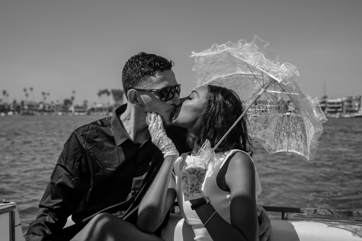 Engaged couple kissing during engagement shoot while riding in the back of a speed boat with the bride to be holding a white lace umbrella.
