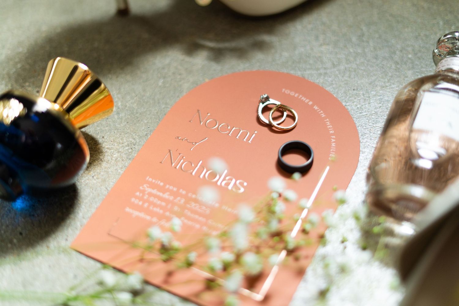 Wedding rings and invitation cards displayed with soft coral and peach tones and floral decor.
