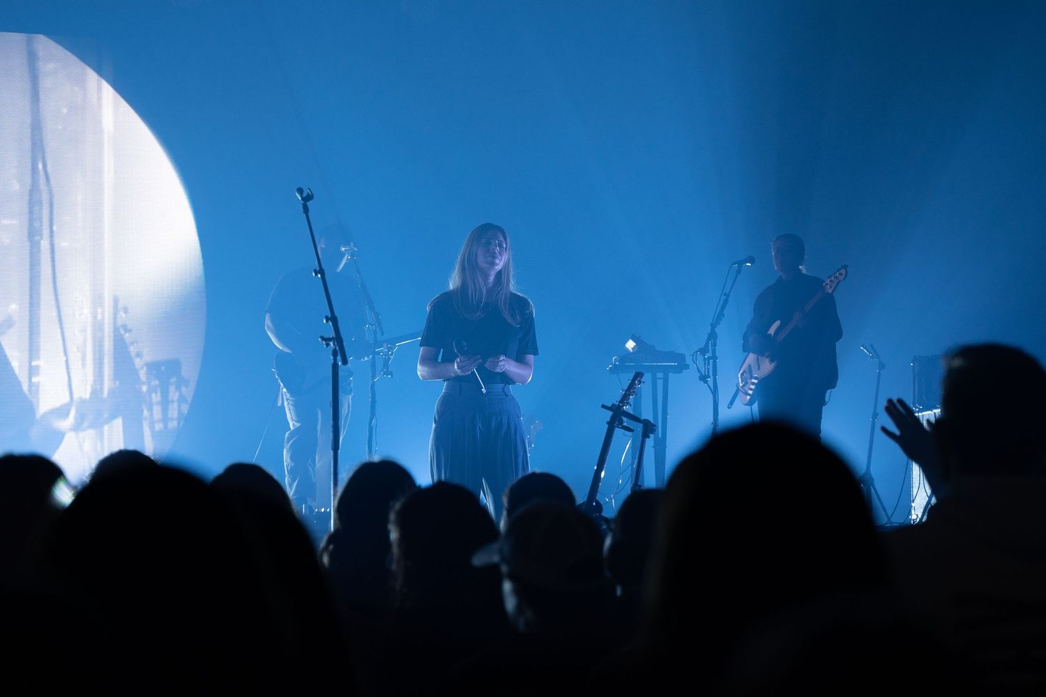 Silhouettes of concert crowd and performers on stage with dramatic blue lighting and fog effects.
