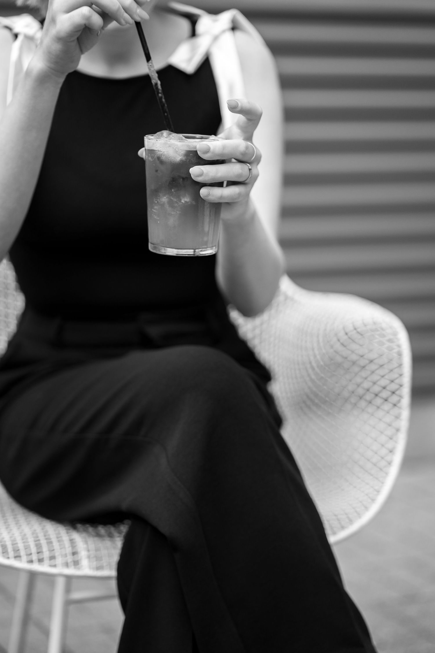 Person in black dress sitting on white chair with drink in hand.