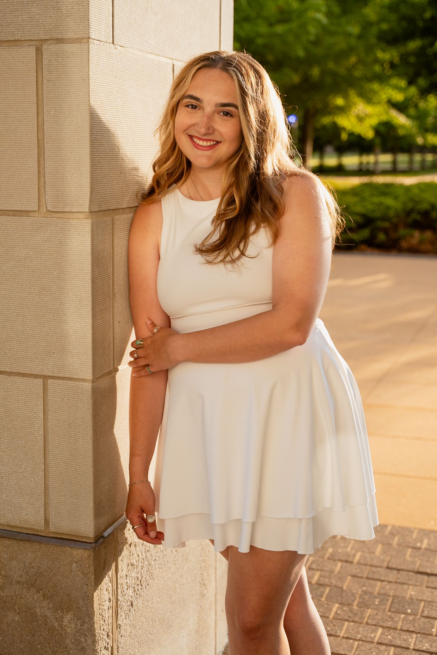 Woman in white dress poses elegantly against architectural columns during golden hour.