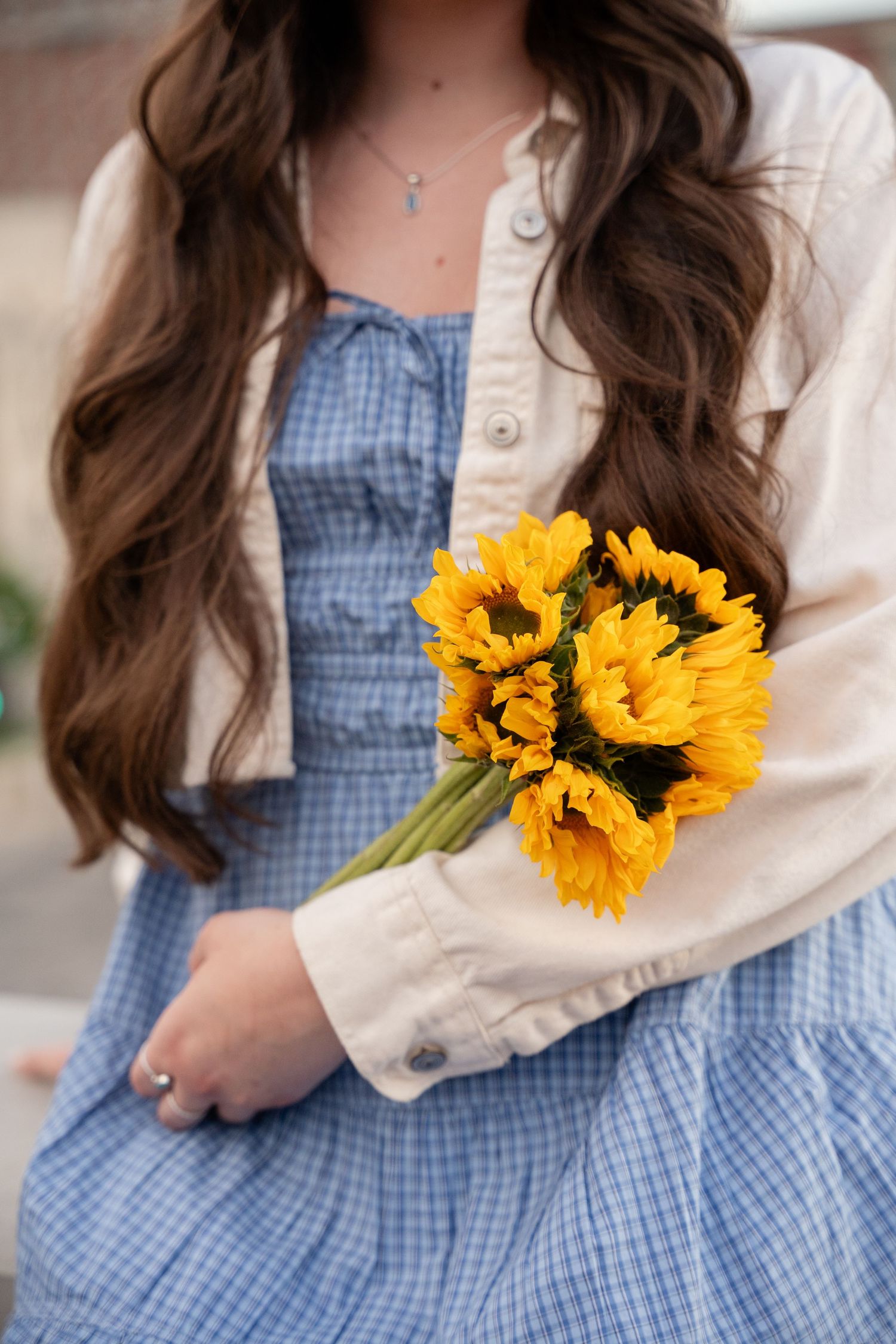 Close-up of blue gingham dress with bright sunflowers and cream cardigan.