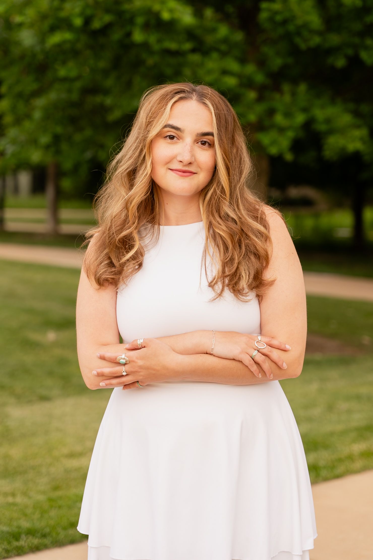 Woman in flowing white dress poses confidently in a sunlit park.