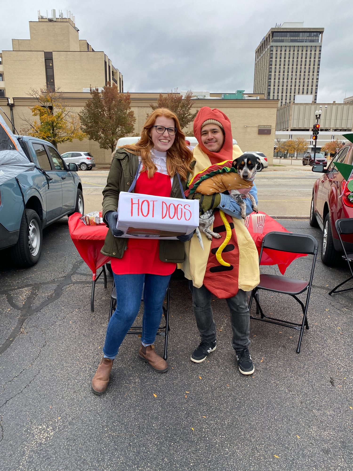 People holding a sign for hot dogs in a parking lot during an outdoor event.
