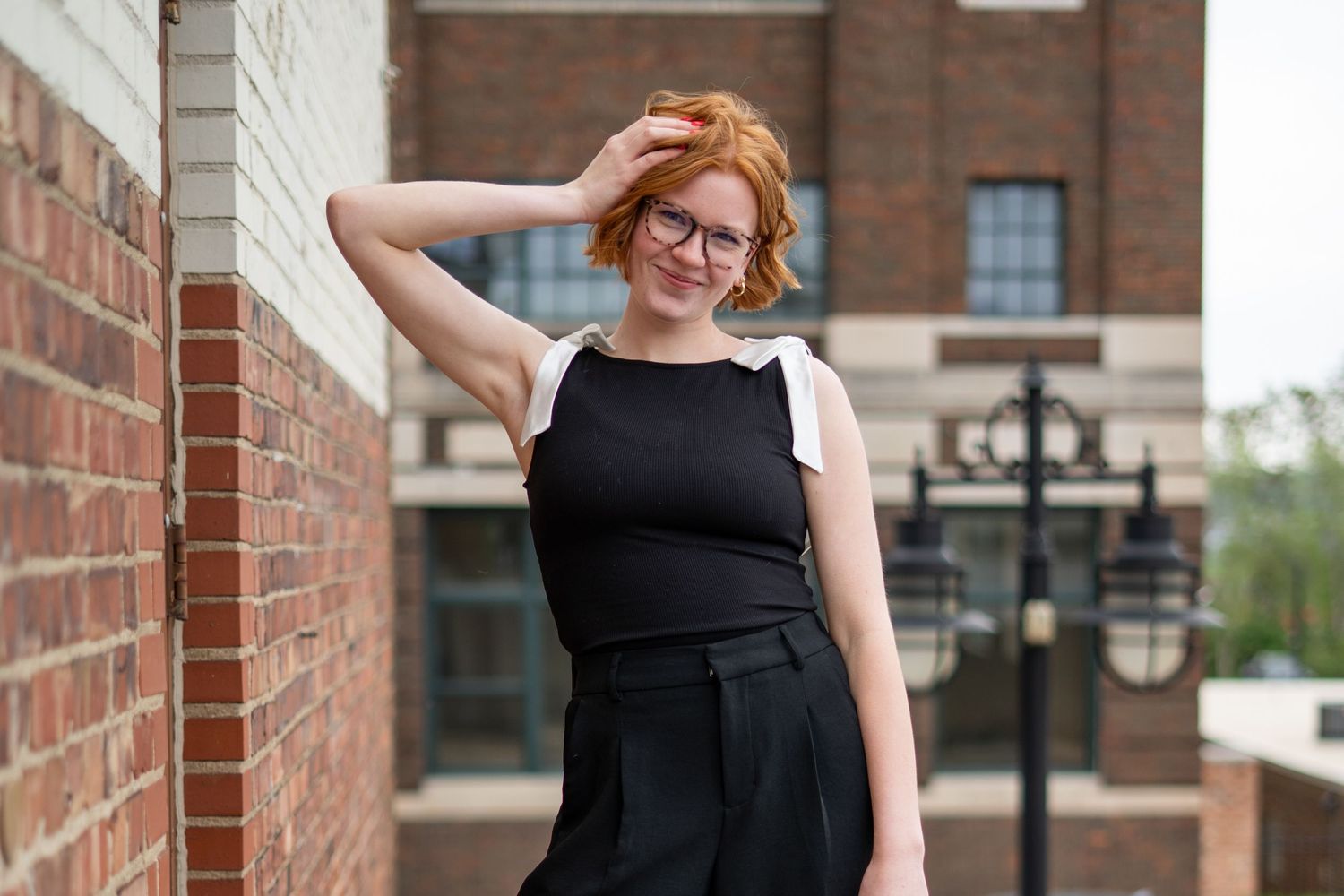 Woman in black dress leans against brick wall with architectural details.