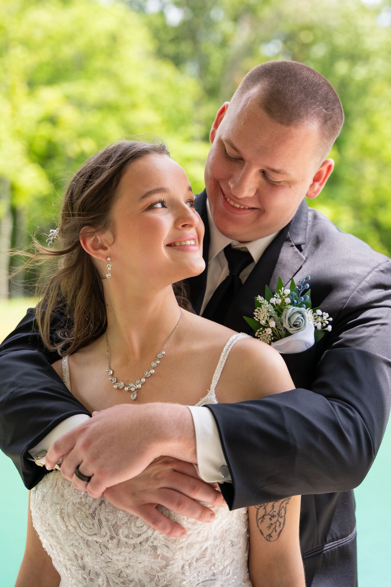 Romantic wedding couple embraces outdoors with joyful laughter in a natural setting.