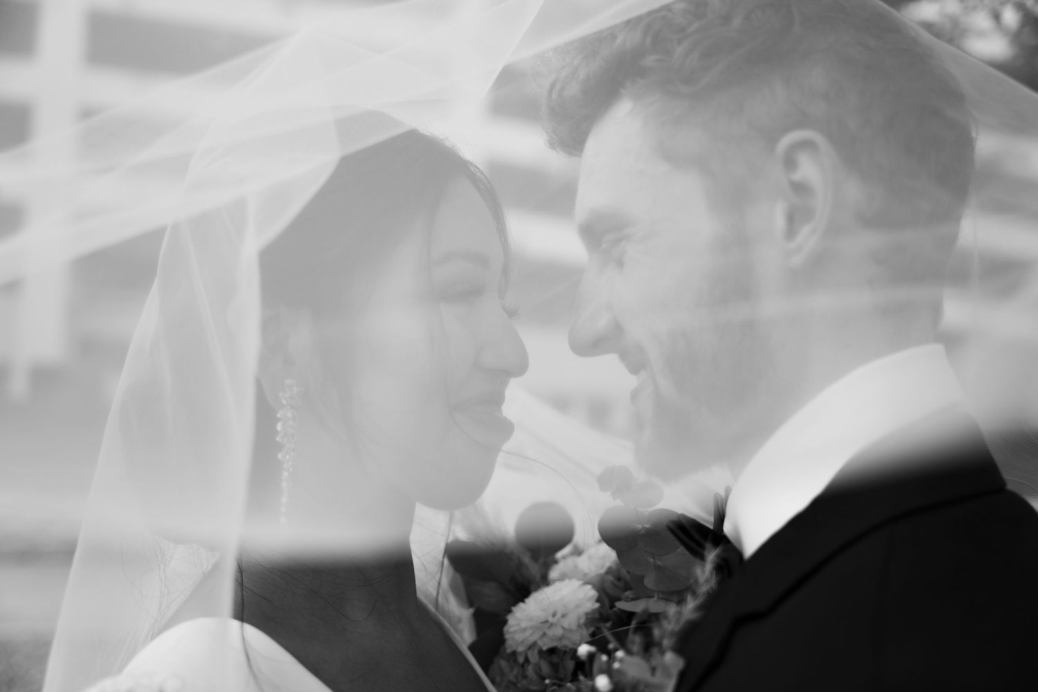 Black and white wedding photograph with romantic veil overlay creating dreamy atmosphere.