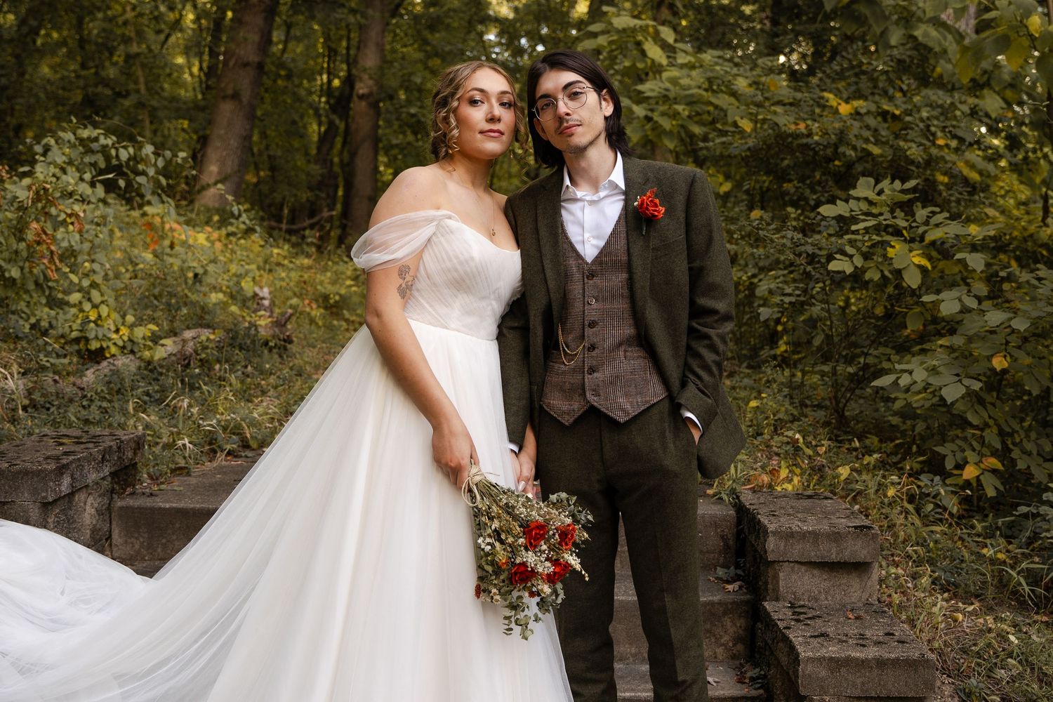 Romantic wedding couple embraces in a lush wooded setting with natural greenery and trees in the background.