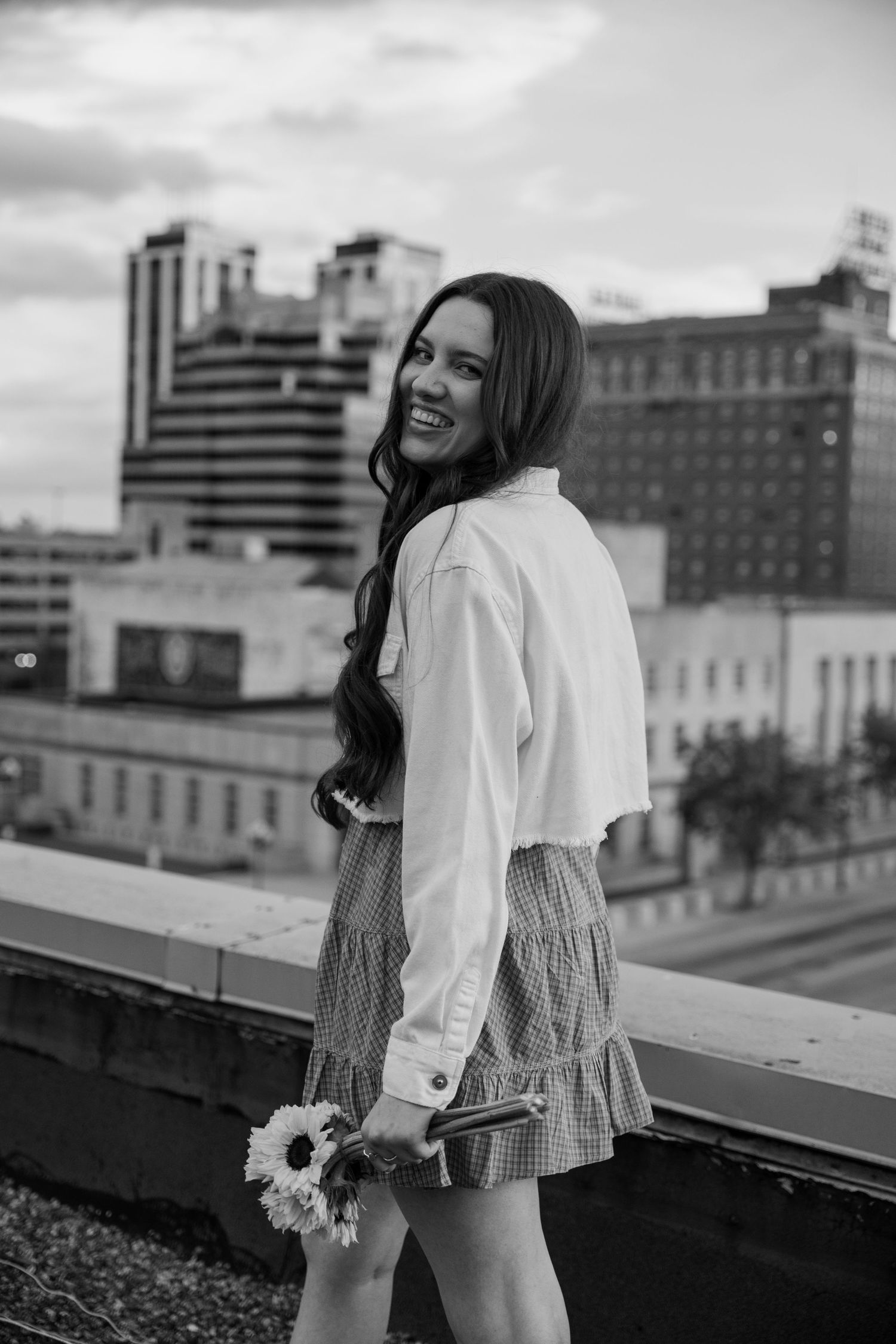 Black and white portrait of person in ruffled top against city rooftops.