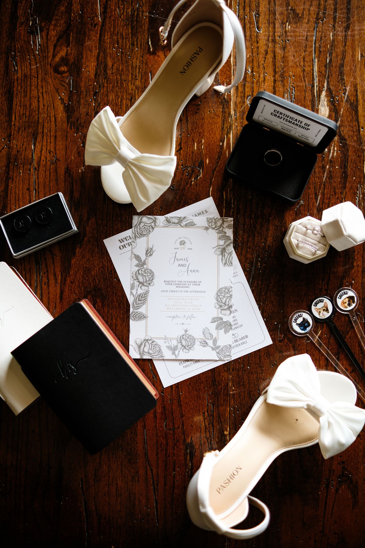 Wedding accessories including white shoes and invitations arranged on wooden surface.
