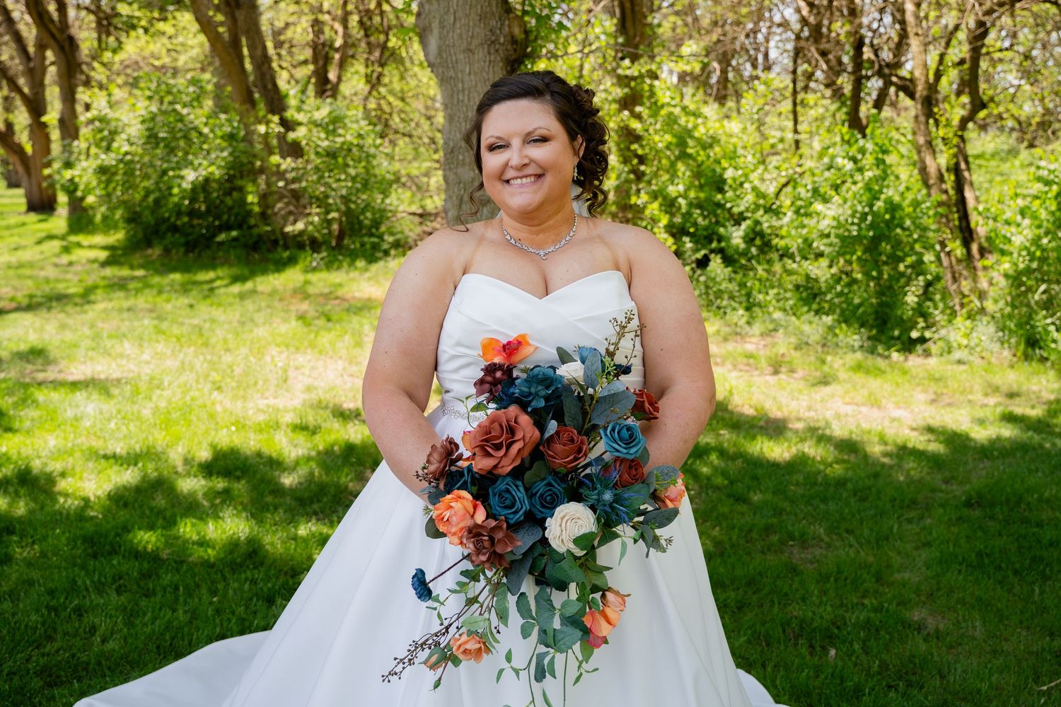 Bride holding colorful bouquet poses in sunny outdoor garden setting.