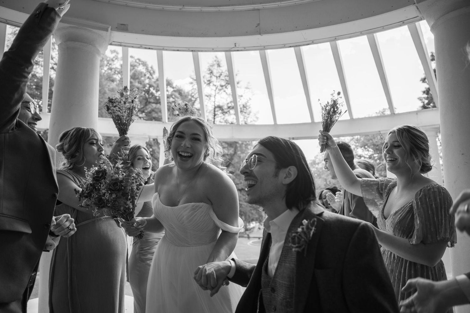 Wedding party celebrating in bright circular room with large windows.