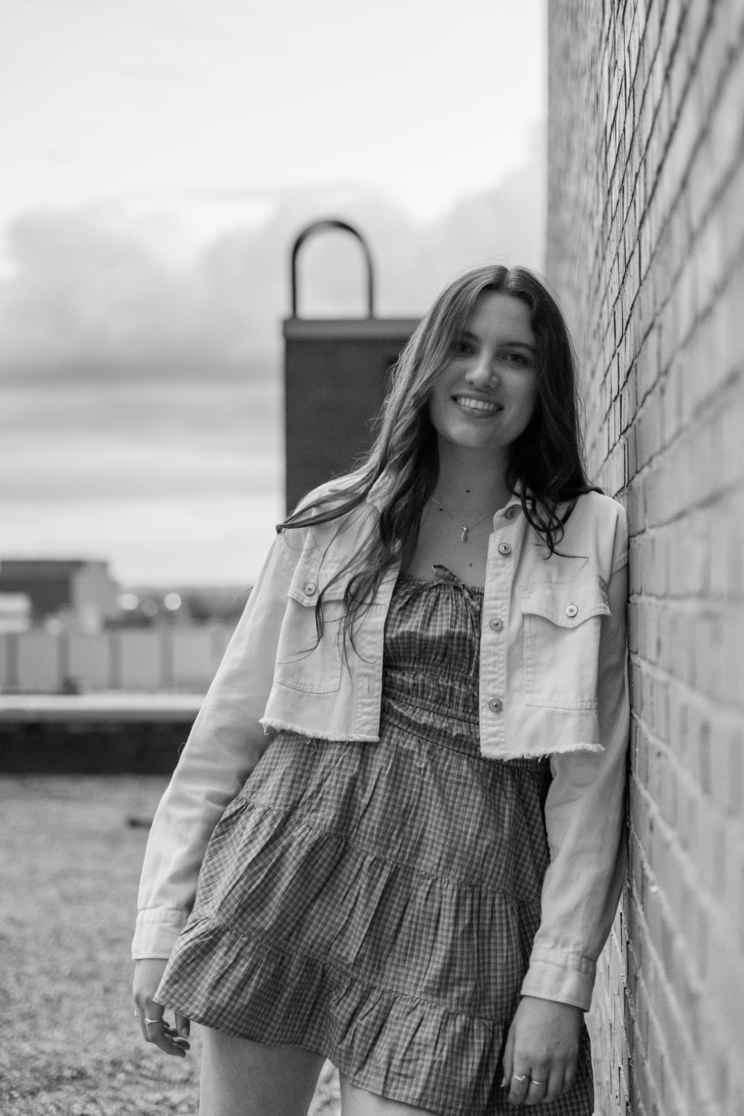 Black and white portrait showing person in checkered dress against brick wall.