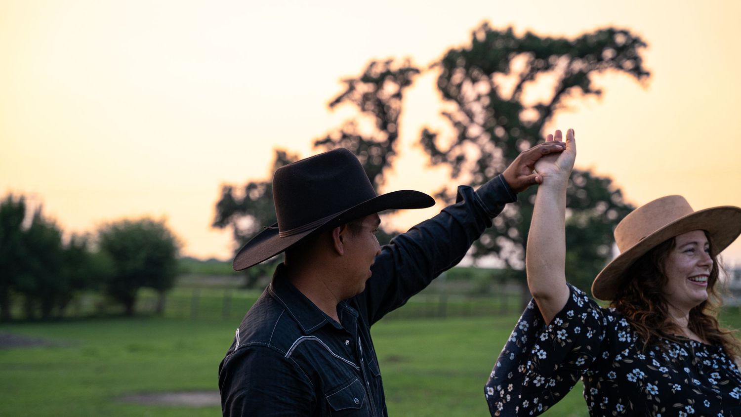 Silhouettes of a couple dance together against a warm sunset sky.