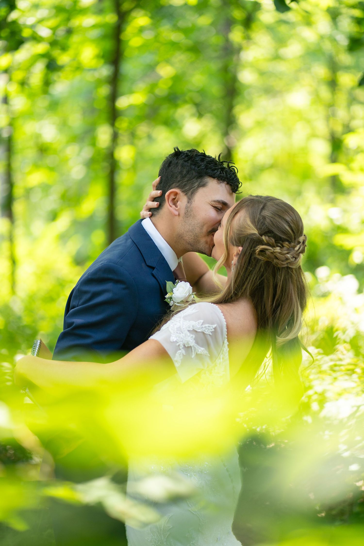 Newlyweds sharing an intimate kiss surrounded by lush green foliage in a garden setting.