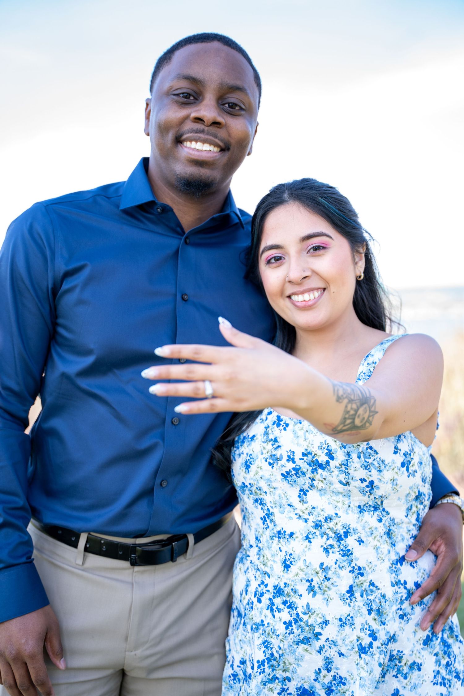 A couple in blue and white outfits poses playfully together outdoors.