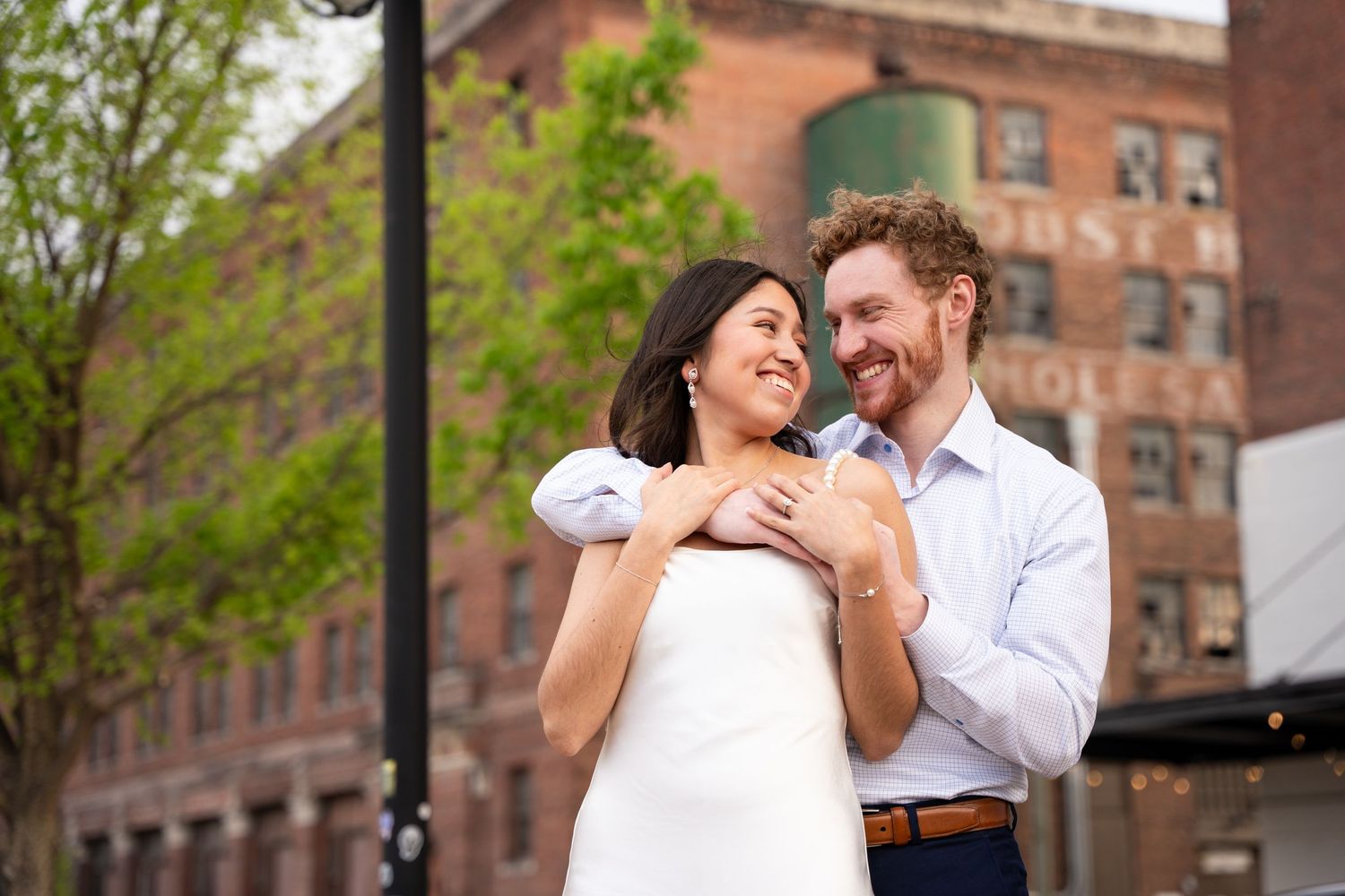A couple shares an intimate moment against a brick building backdrop in an urban setting.