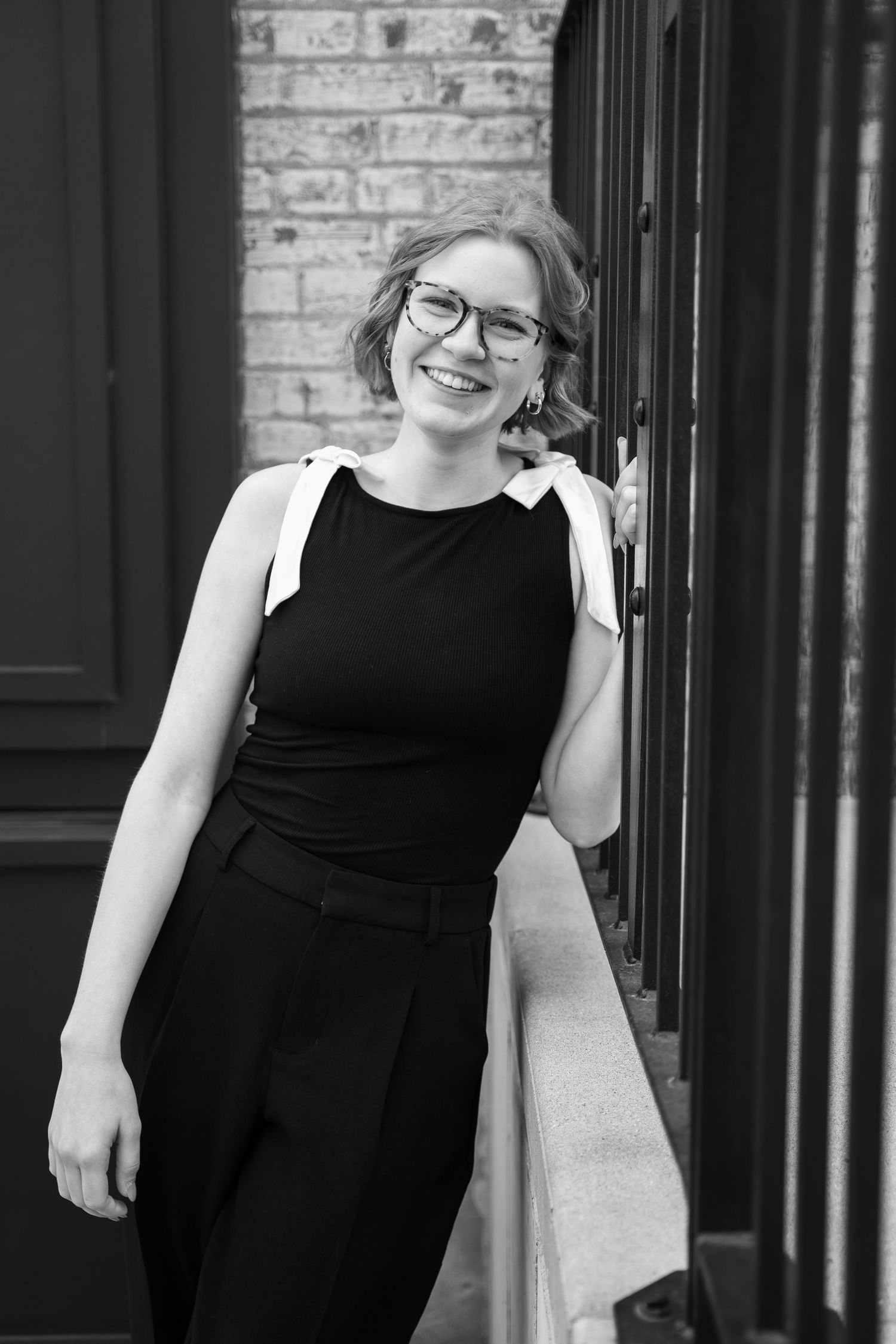 Person in black dress poses casually against brick wall backdrop.