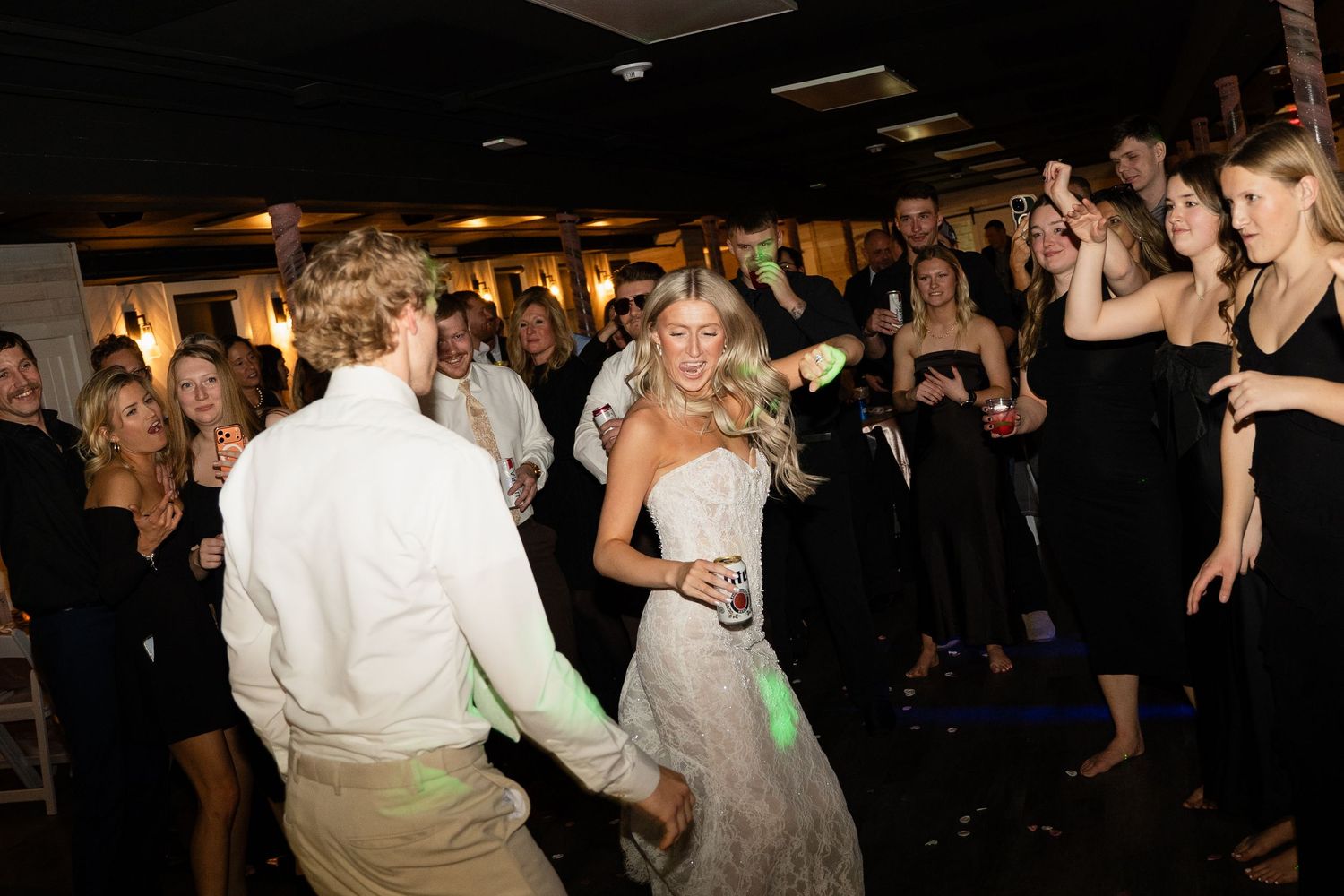 A group of people dancing and celebrating at a dimly lit party or reception venue.