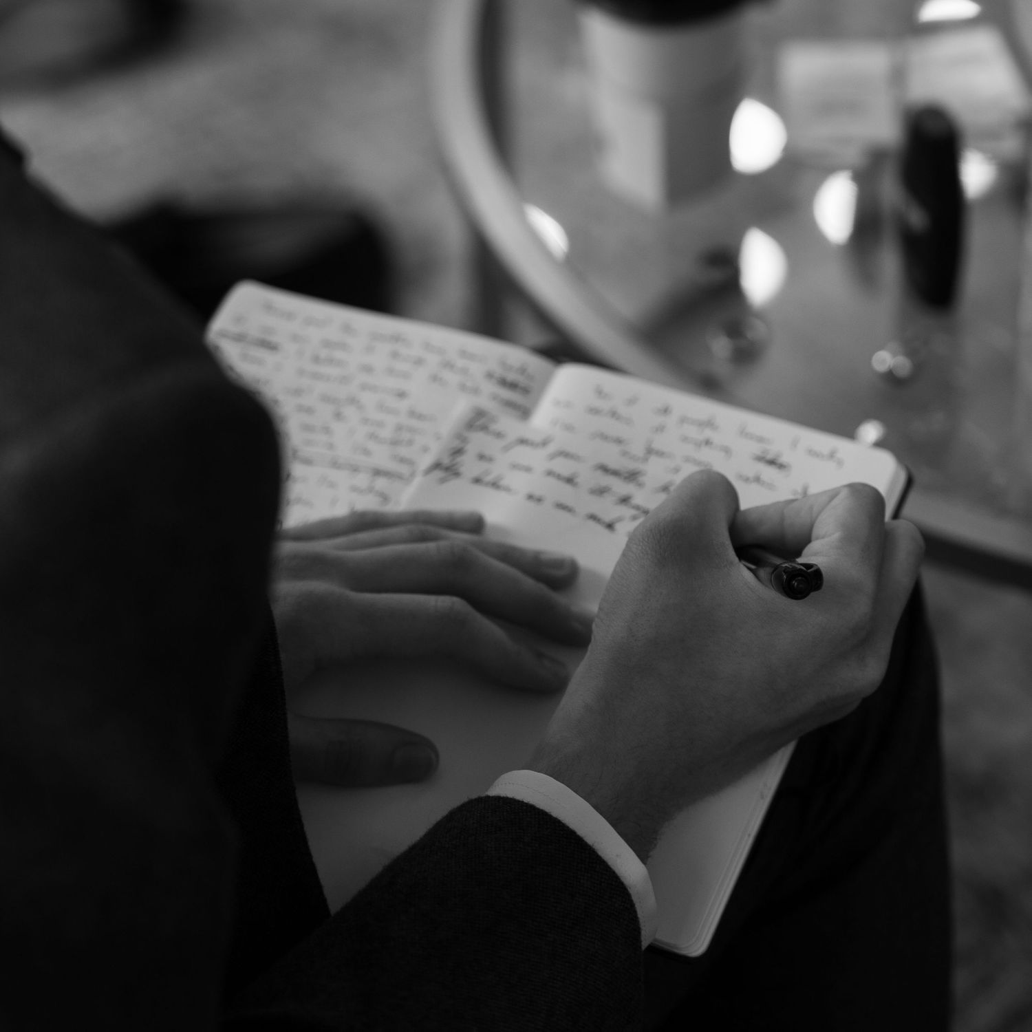 Close-up of hands writing on paper in black and white.