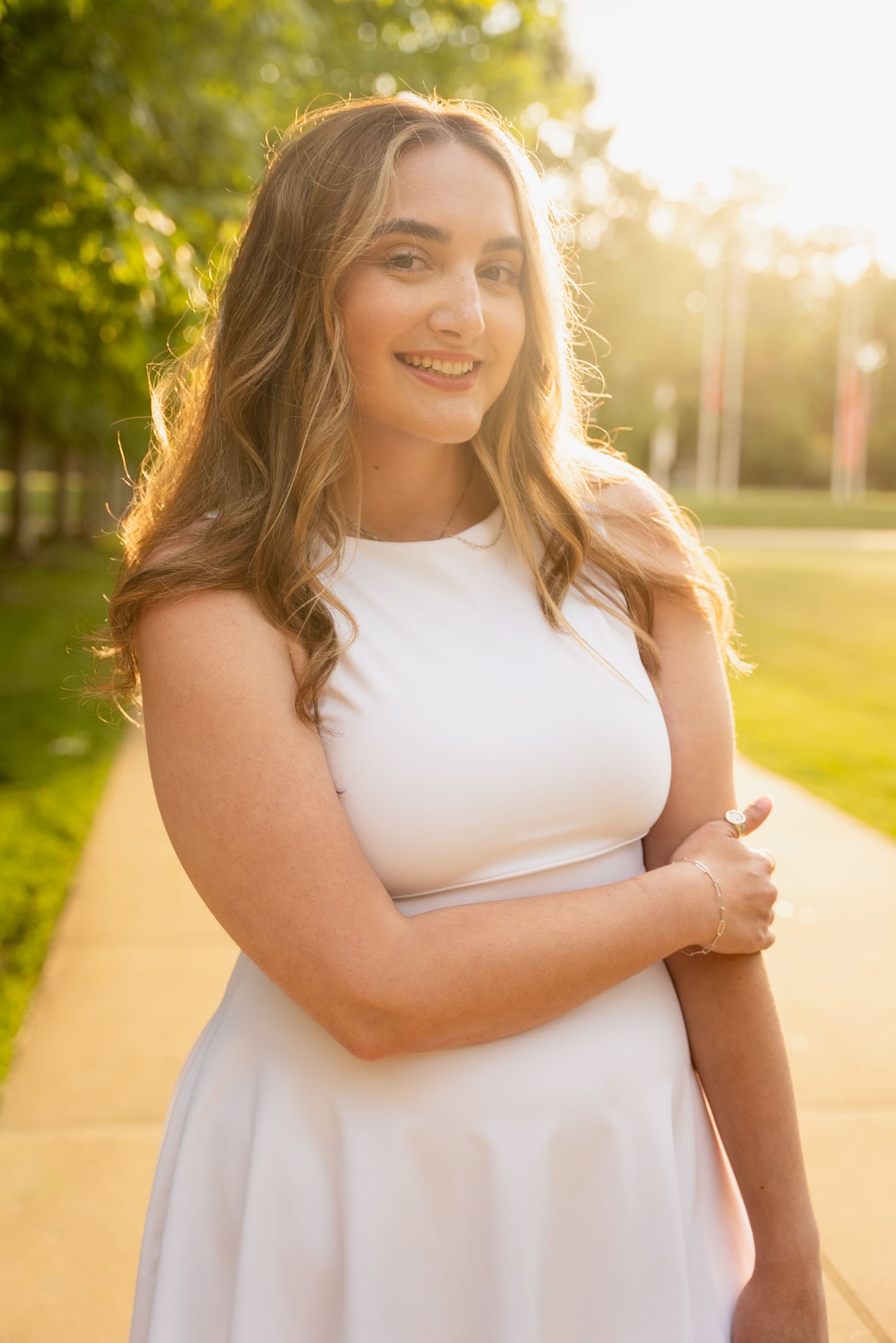 Woman in white sleeveless dress poses gracefully during golden hour in a park setting.