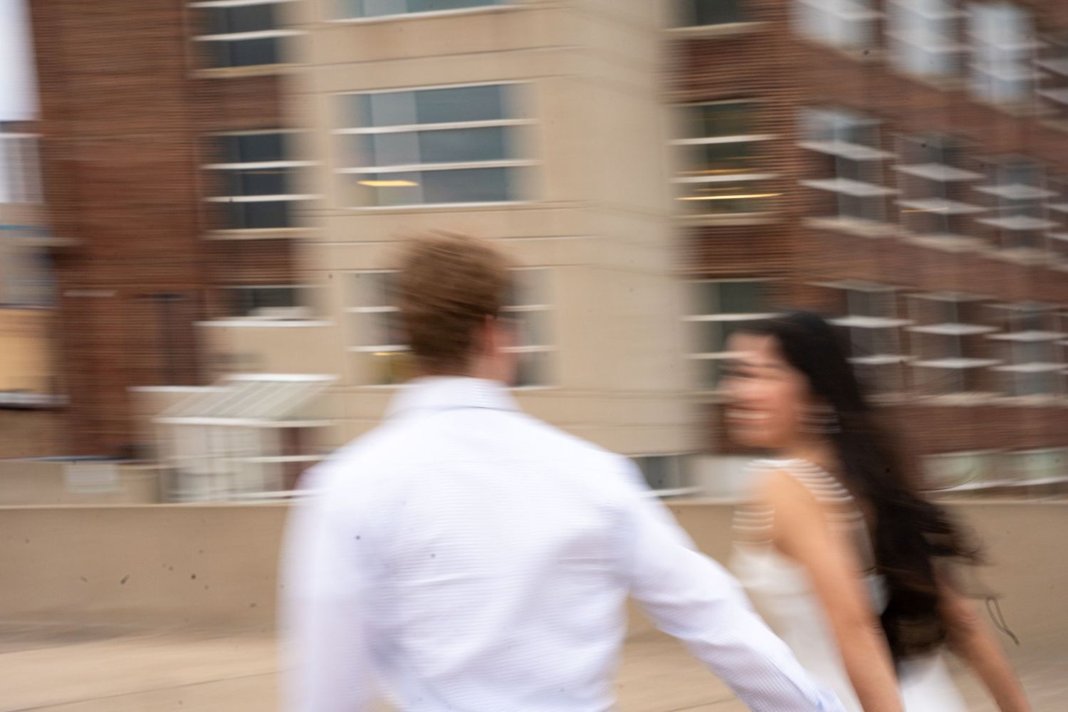 A couple in coordinated white outfits dances together in front of an urban backdrop.