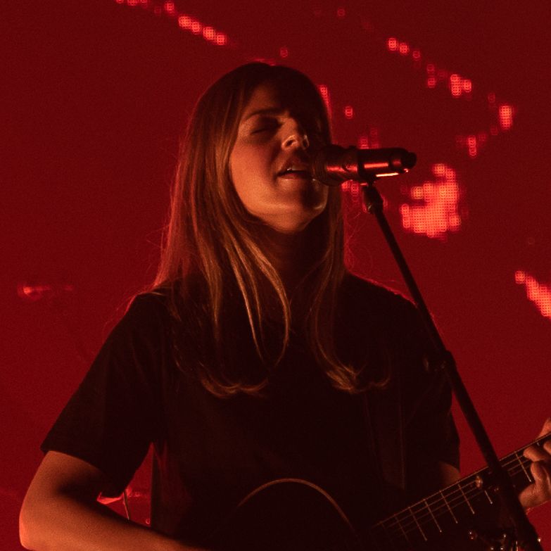 Musician performing on stage bathed in dramatic red lighting.