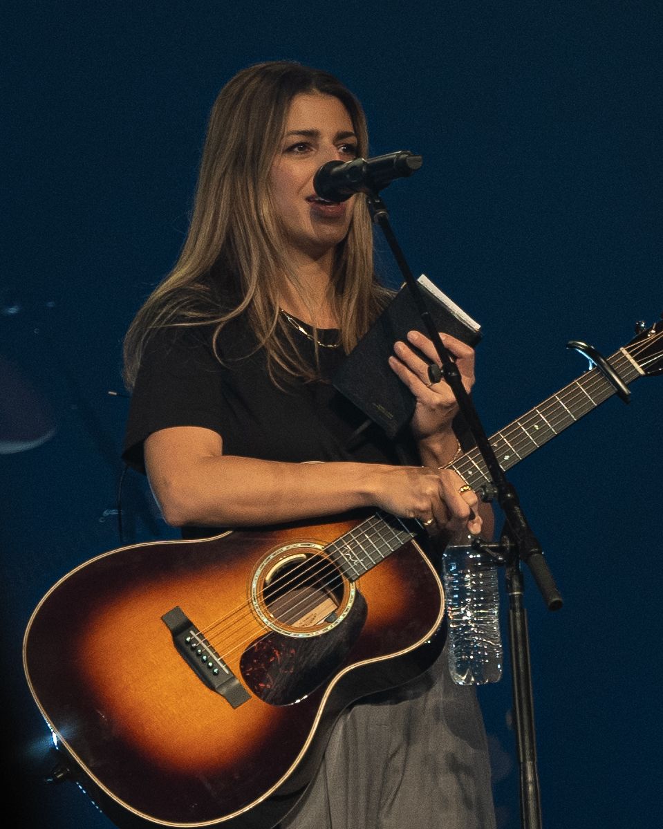 Musician performing on acoustic guitar with sunburst finish under stage lighting.